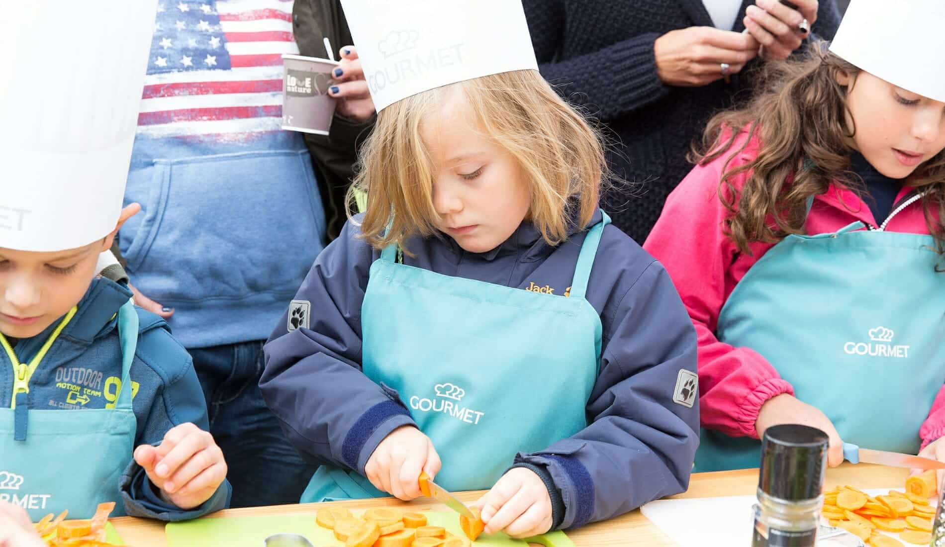 Gesunde Jause Kinder mit Kochhaube beim Karottenschneiden