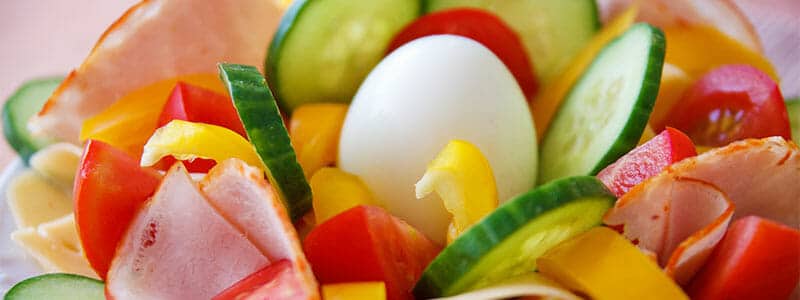 Ein Salat mit Gurken, Tomaten, gelber Paprika, Schinken und Ei macht satt und ist gesund.