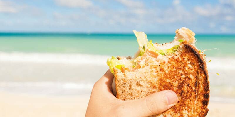 Hand mit Snack am Strand mit Meer im Hintergrund