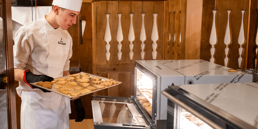 Lehrling schiebt Kekse in den Ofen bei der Gourmet Backwerkstatt